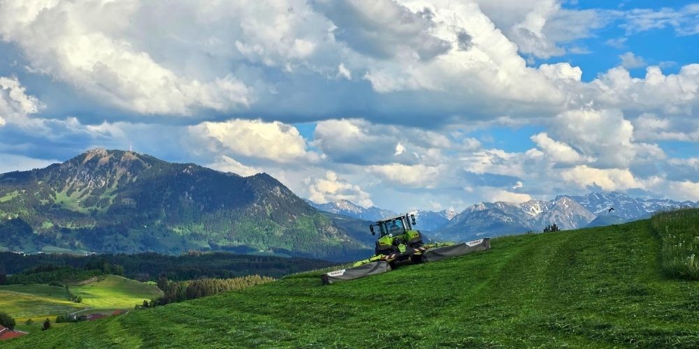 Traktor auf grüner Wiese vor Alpenpanorama beim Bauernhofurlaub auf dem Ferienhof Eger in Bayern