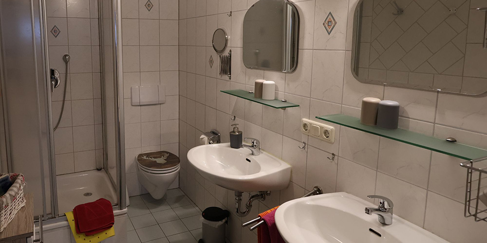 Badezimmer der Ferienwohnung Grüntenblick mit Dusche, 2 Waschbecken, Kosmetikspiegel & Fön – sauber, hell und komplett ausgestattet