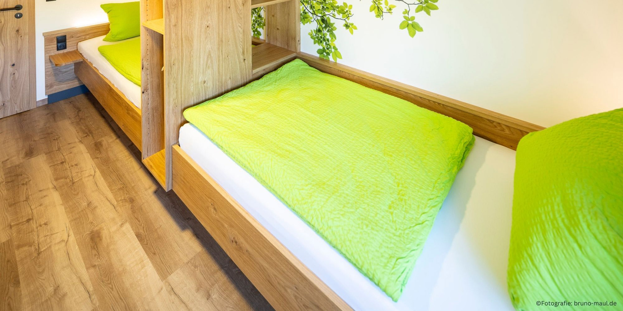 Helles Kinderzimmer mit zwei großen Einzelbetten, Regal, Spielecke und Wandmotiv mit Blättern – Ferienwohnung Morgensonne im Allgäu