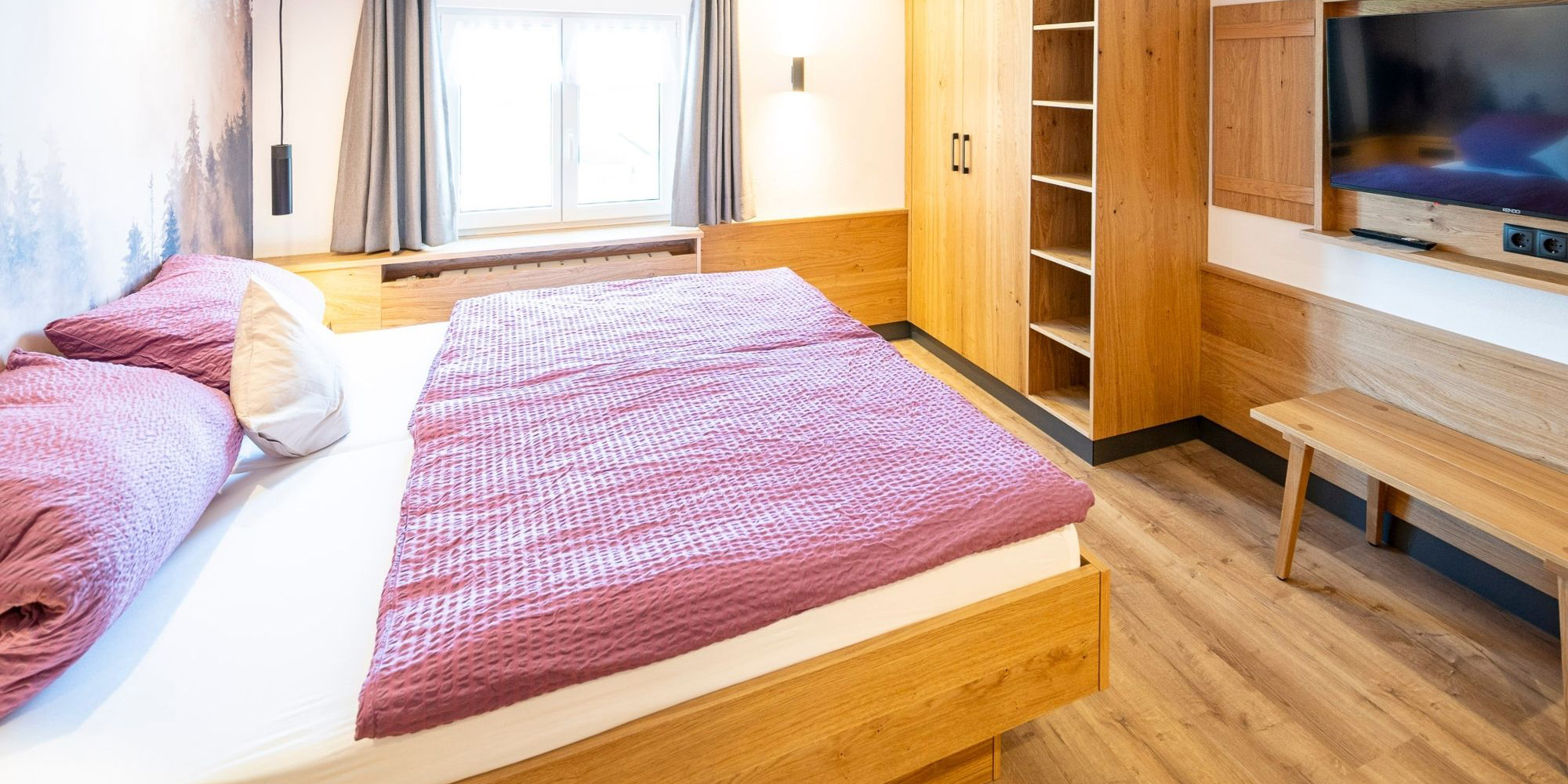 Helles Schlafzimmer im gemütlichen Landhausstil mit Holzbettrahmen, Schrank und TV – Ferienwohnung Morgensonne im Allgäu