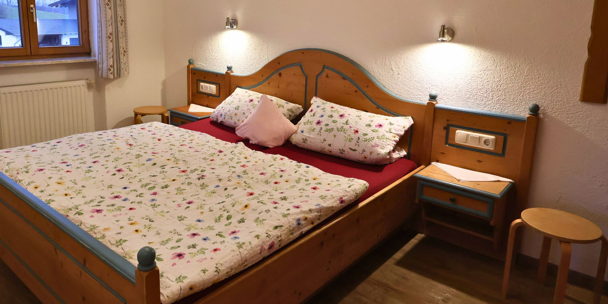 Erstes Schlafzimmer der Ferienwohnung Waldblick mit Doppelbett, Leselampen und Fensterblick – ideal für Eltern im Allgäu-Urlaub