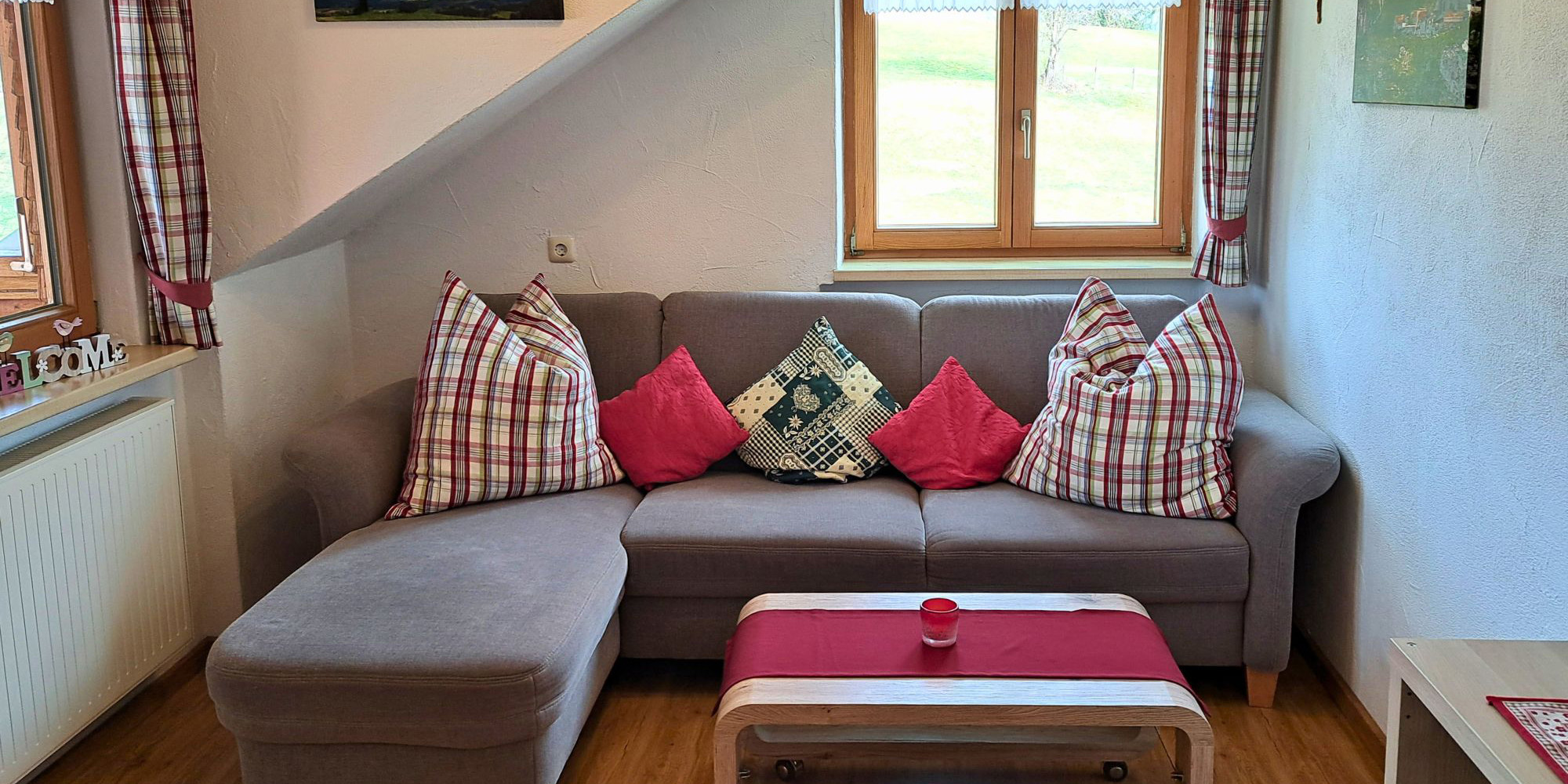 Gemütliches Wohnzimmer der Ferienwohnung Waldblick mit Sofa, Kissen & Fensterblick – ideal für Familienurlaub im Allgäu