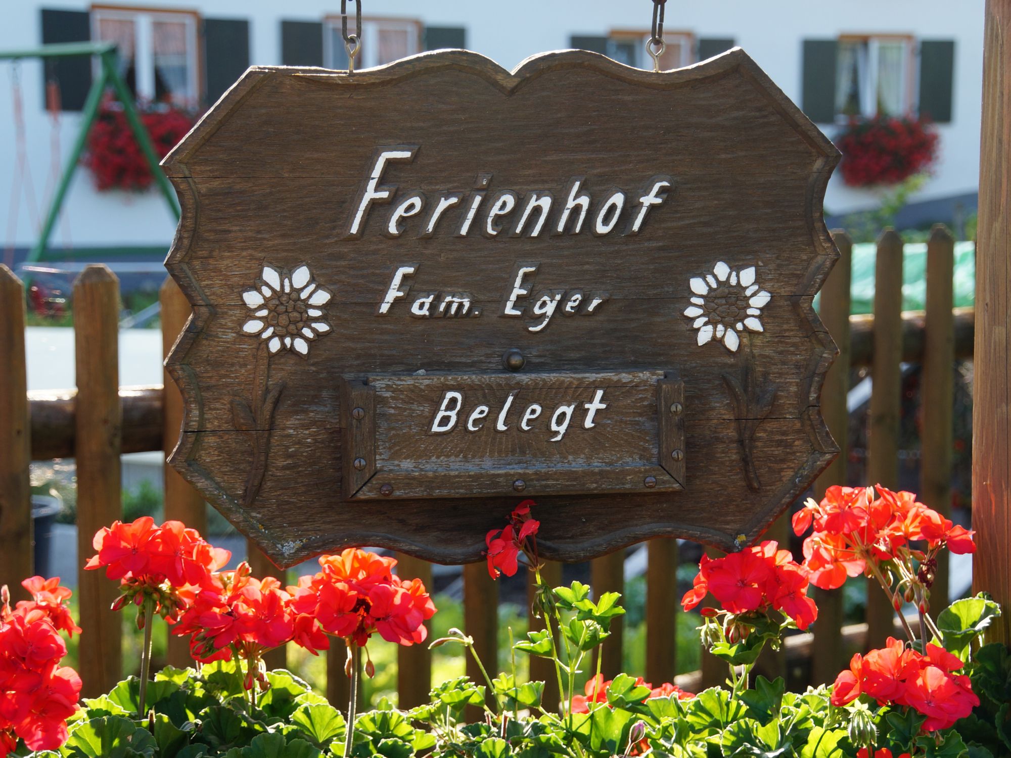 Hofschild des Ferienhofs Eger mit den Ferienwohnungen Waldblick und Grüntenblick und Morgensonne – liebevoll gestaltet, umrahmt von roten Geranien