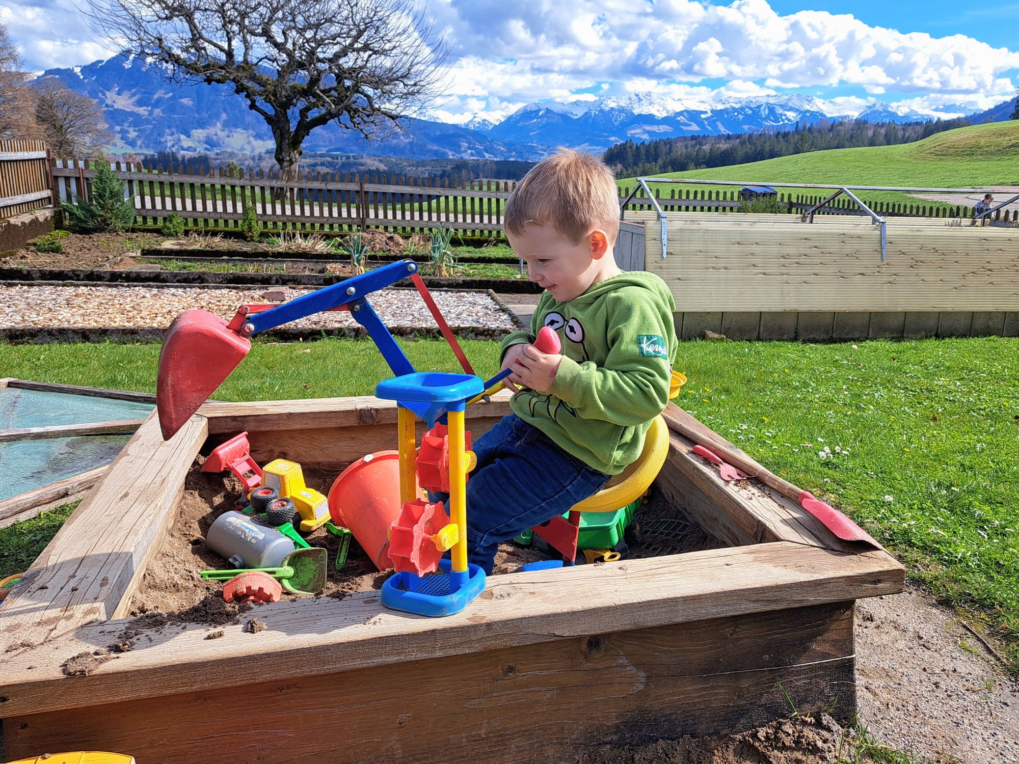 Kleinkind spielt im Sandkasten auf dem Ferienhof Eger – sicherer Spielbereich mit traumhaftem Blick in die Allgäuer Alpen