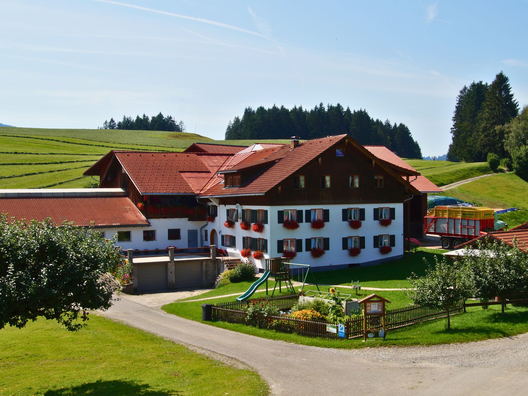 Ferienhof Eger im Allgäu bei Sonnenschein – traditionelle Außenansicht mit Blumen, Hofzufahrt und ruhiger Lage zwischen Hügeln